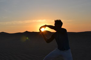 Person creating the illusion of holding the sun between their hands at sunset in a desert.